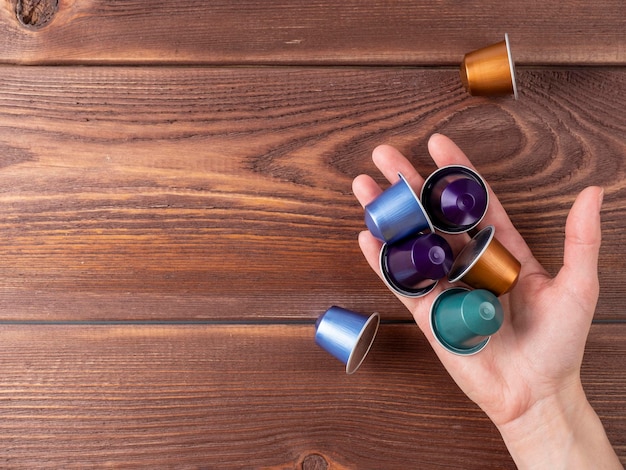 Una mano tiene una manciata di capsule di caffè colorate su uno sfondo di legno marrone. vista dall'alto, copia spazio,
