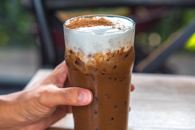 Hand hold iced chocolate or cocoa latte in glass