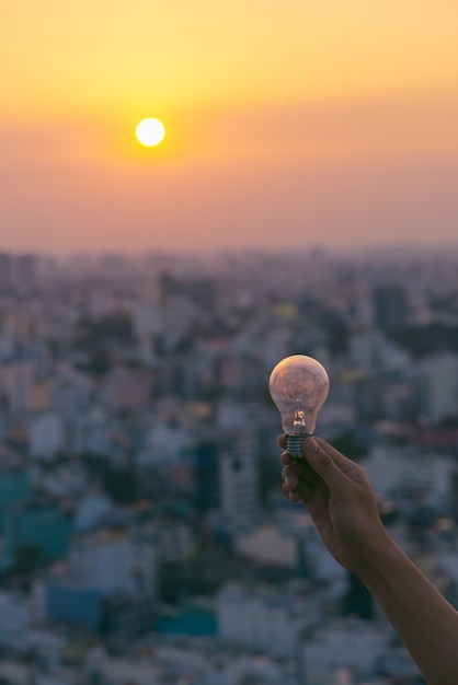 Hand hold a light bulb on sunset background for saving energy and creative concept.