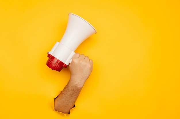 Hand hold megaphone up isolated through torn yellow background