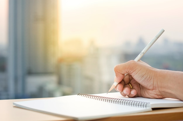 Hand hold pencil writing on note book with blur sunset background.