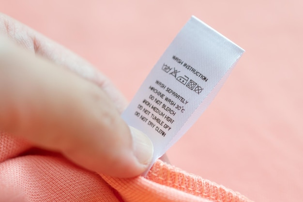 Hand hold and reading at white laundry care washing instructions clothes label on pink shirt