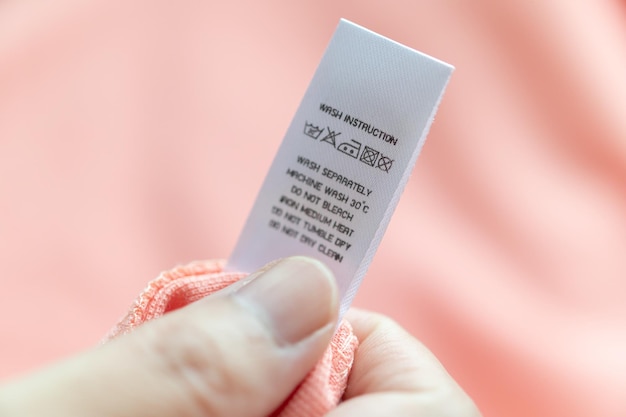 Hand hold and reading at white laundry care washing instructions clothes label on pink shirt