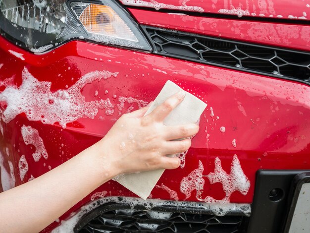 Hand hold sponge over the red car for washing