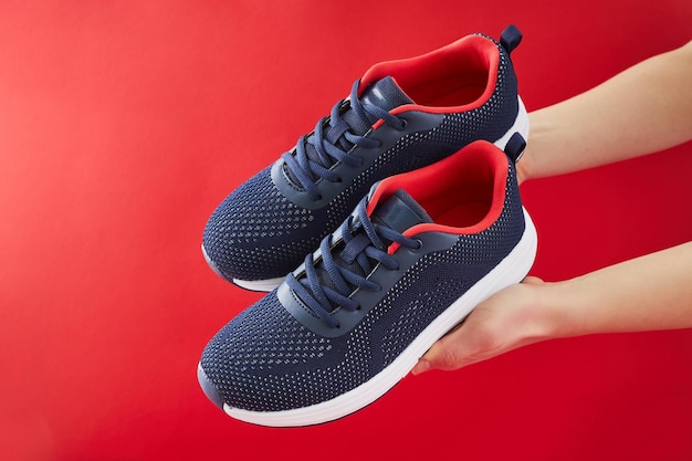 Hand hold sports shoes on red background Choosing and buy of new sneakers