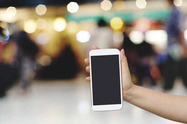 Hand hold and touch screen with Blur shopping mall background.