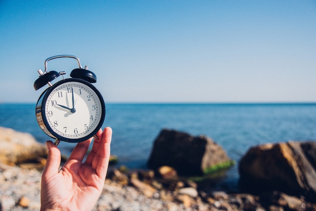 Hand hold watch on beach background.Alarm clock on sea and sand background different time with summer vacation.Vacation time concept.