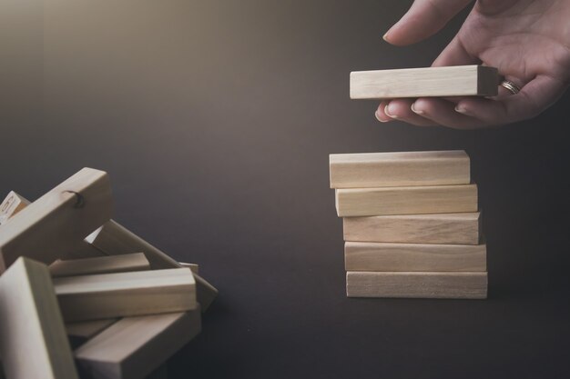 Hand hold a wooden block under stack of the same blocks. Business conceptual image