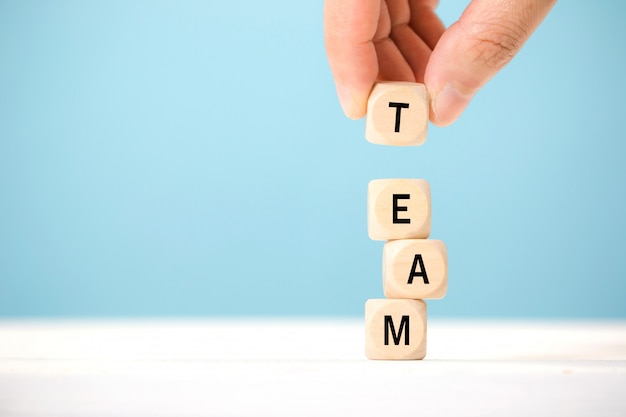 Hand hold wooden cube elements with letter on wooden table, which represents team. Business concept.