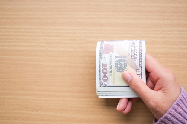 Hand holding 100 dollas bank note with sweater on wooden table