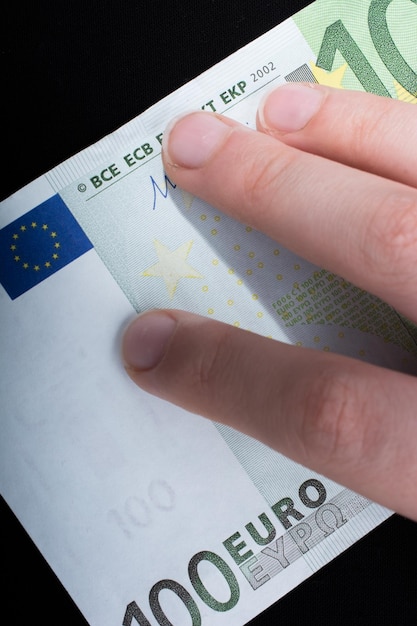 Hand holding 100 euro banknote on a black background