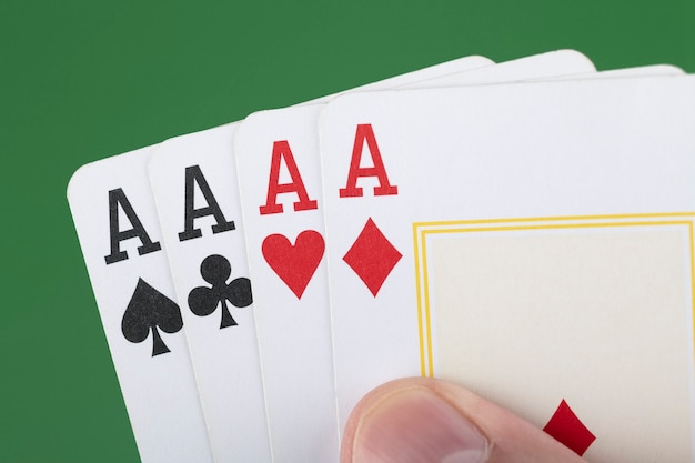 Hand holding 4 aces cards over green background.