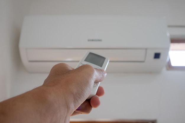 Hand holding AC remote control directed on the air conditioner inside the room