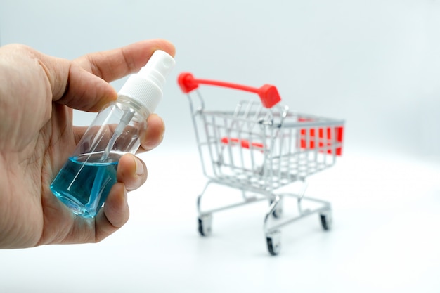 Foto mano che regge un flacone spray alcolico per la disinfezione sulla maniglia del carrello del supermercato per la sicurezza da sporco e batteri.