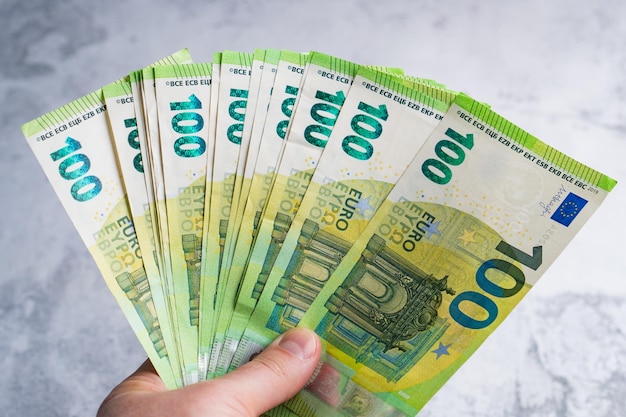 Фото Рука держит и дает сто банкнот по 100 евро вентилятор денег в мужских руках на сером фоне