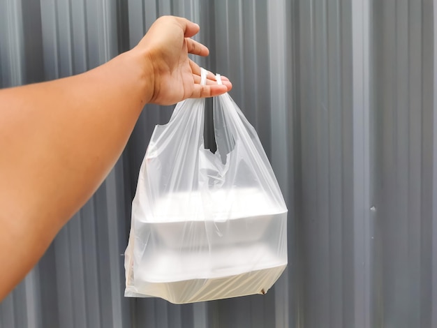 Hand holding a bag of take away food in polystyrene container.