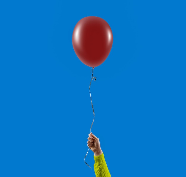 Hand holding balloon against clear blue sky