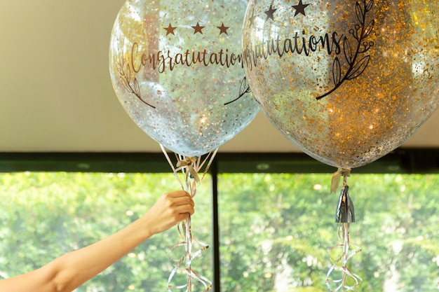 Hand holding balloons with  Congratulation text on it at party decoration.