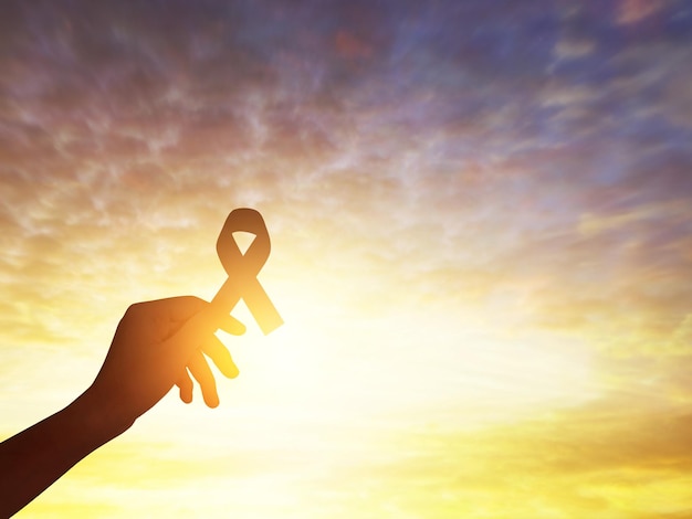 Hand holding black awareness ribbon at sunset sky