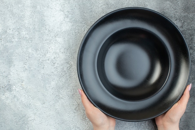 Hand holding black dinnerware set on the left side on isolated gray ice surface with free space