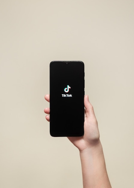 A hand holding a black phone with the logo of tik tok app on the screen