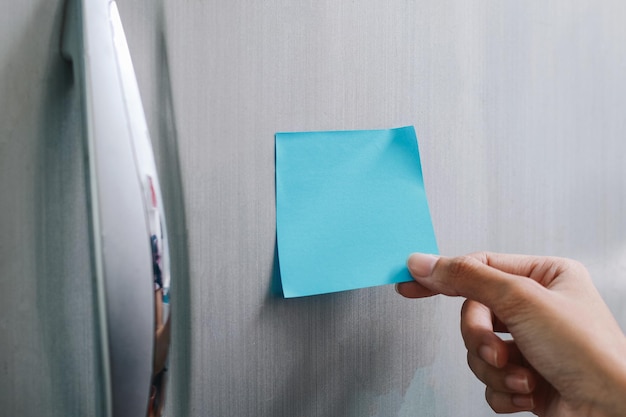 Hand holding a blank blue sticky notes in refrigerator door