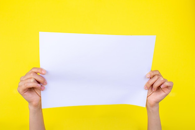 Hand holding blank paper on isolated yellow background. Closeup photo of empty white paper.