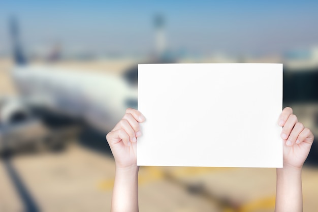 Hand holding blank paper with airplane blurred background