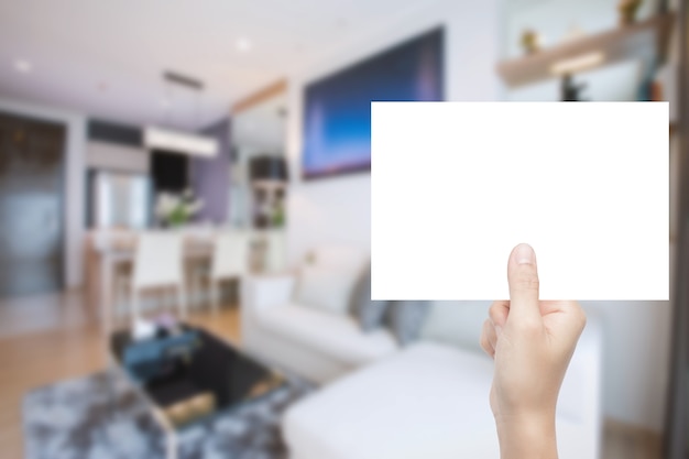 Hand holding blank paper with home interior blurred background