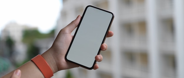 Hand holding blank screen smartphone while standing at balcony