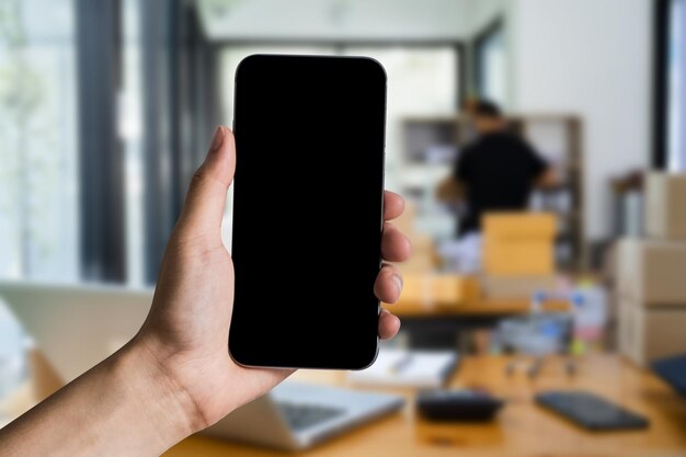 Hand holding blank smartphone with blank screen in office