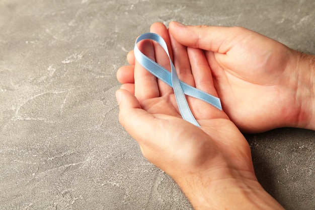 Hand holding blue breast cancer ribbon on grey surface