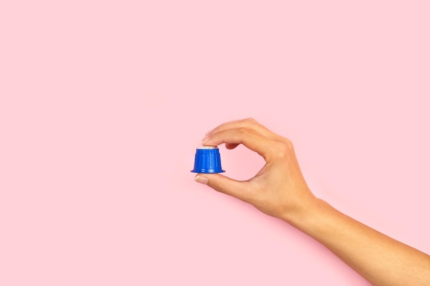 A hand holding a blue cappuccino cap on a pink background