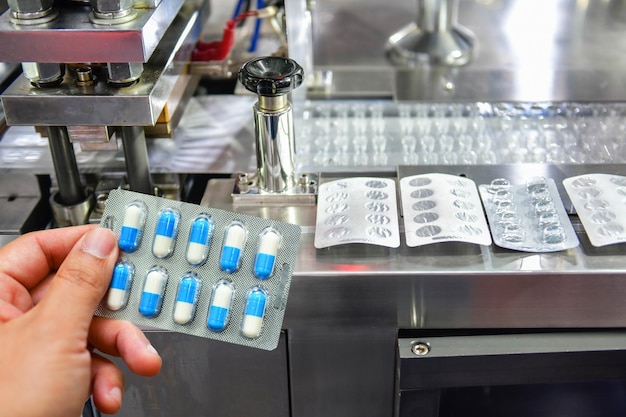 Hand holding blue capsule pack at medicine pill production line Industrial