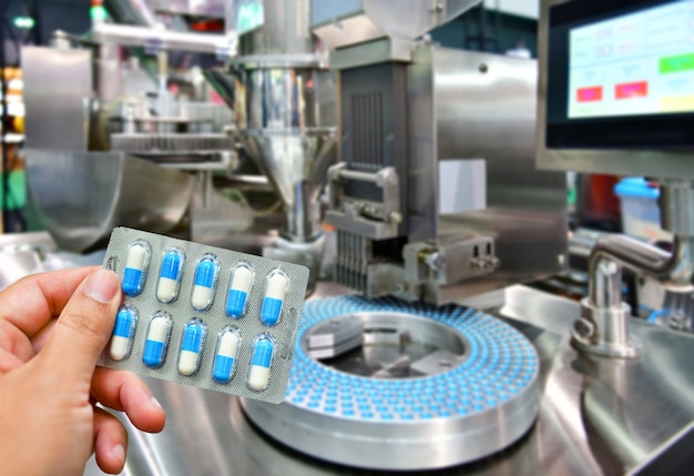 Foto mano che tiene il pacchetto di capsule blu alla linea di produzione della pillola della medicina