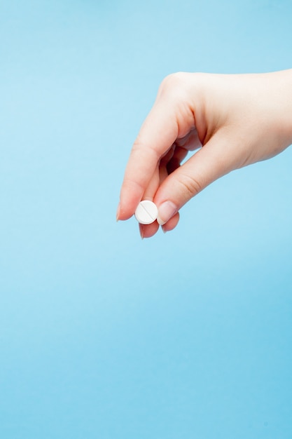 Hand holding a blue pill on a blue background