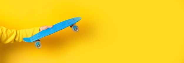 Mano che tiene il skateboard blu su giallo