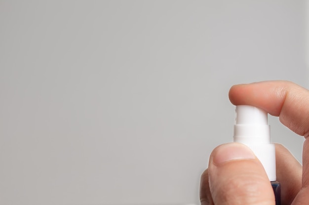 Hand holding a blue spray bottle on gray background.