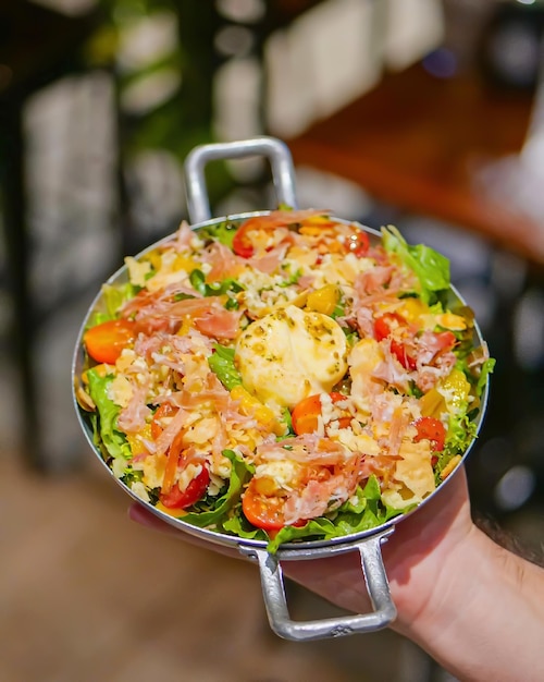 A hand holding a bowl of salad with a salad in it