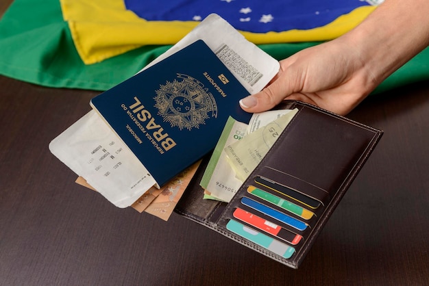 Hand holding Brazilian passport over table with Brazilian flag in the background