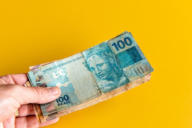 Hand holding brazilian real money notes on yellow background