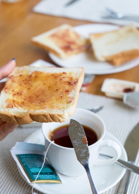 Hand holding bread with fruit jam and tea cup on wood table