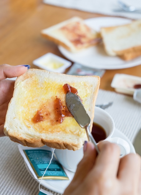 Hand holding bread with fruit jam and tea cup