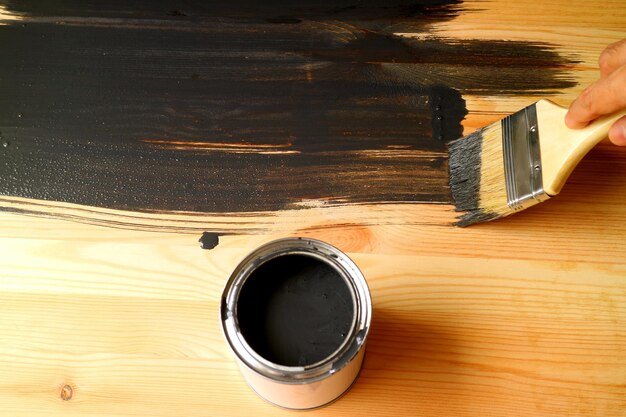 Hand holding brush painting the surface of wood plank