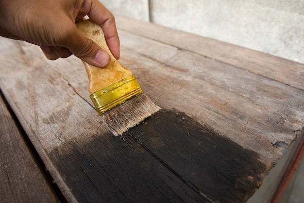 Mano che regge una spazzola la pittura di tavole di legno in legno superficie con macchia di legno