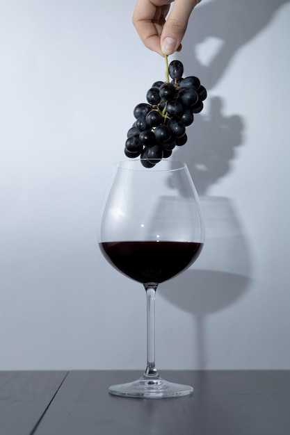 Hand holding bunch of grapes above glass of red wine Selective focus