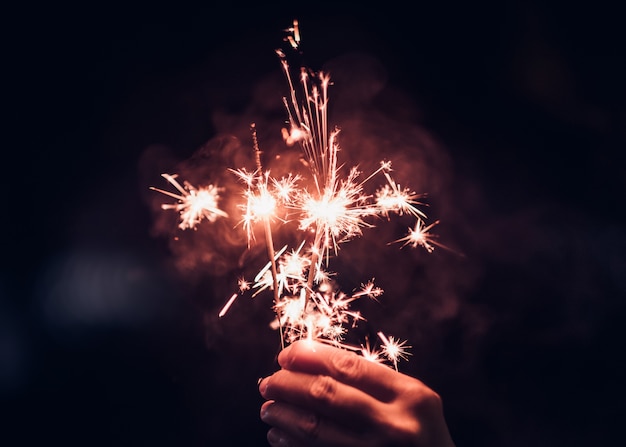 Hand holding burning Sparkler blast on a black