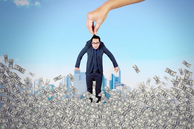 Hand holding a businessman above stack of money