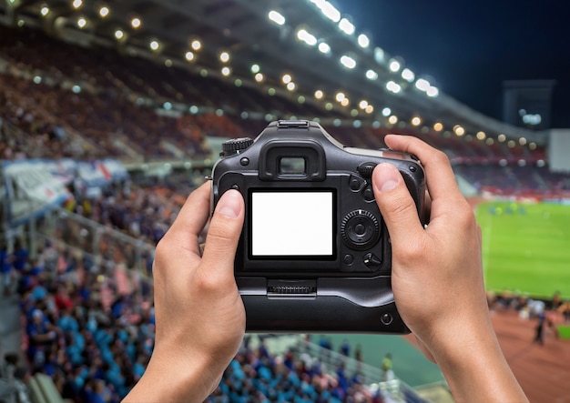 Mano che tiene la fotocamera sopra folla foto astratta offuscata di spettatori su uno stadio