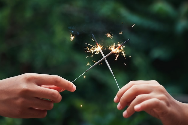 Mano che tiene il fuoco d'artificio di candela su sfondo verde